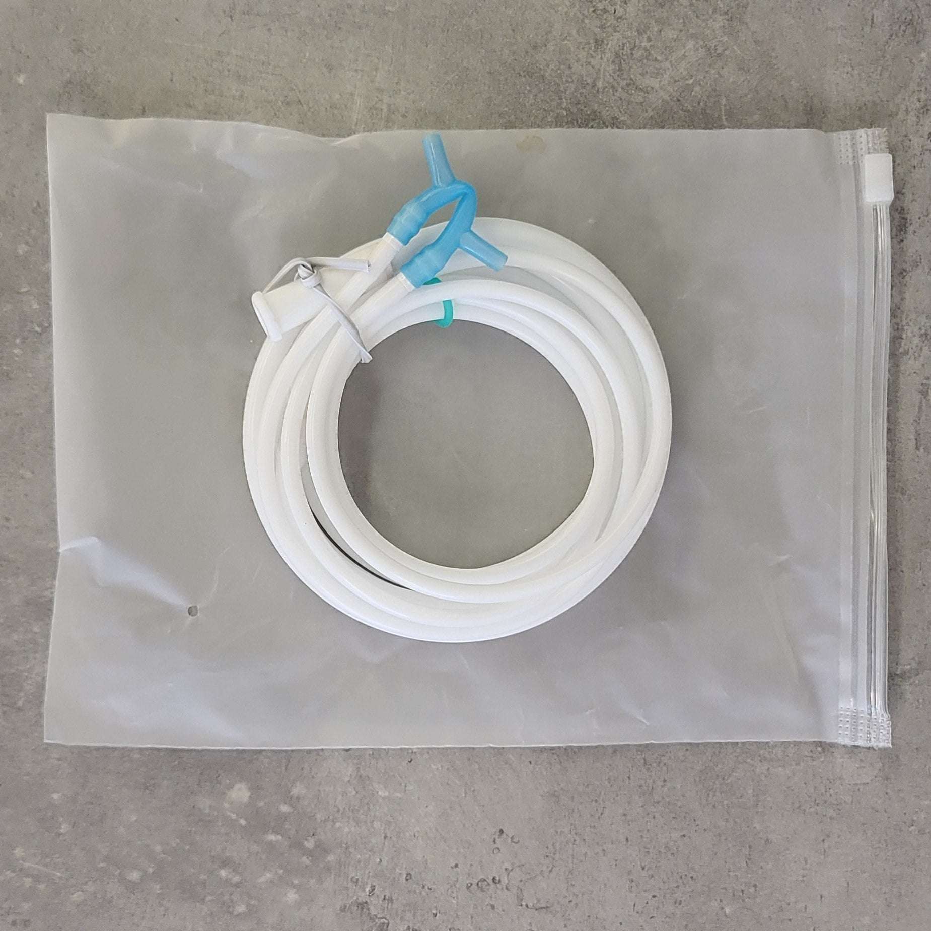 Ein weißer, aufgerollter Schlauch mit blauen und weißen Verbindungsstücken liegt auf einem transparenten Beutel mit Zipperverschluss.