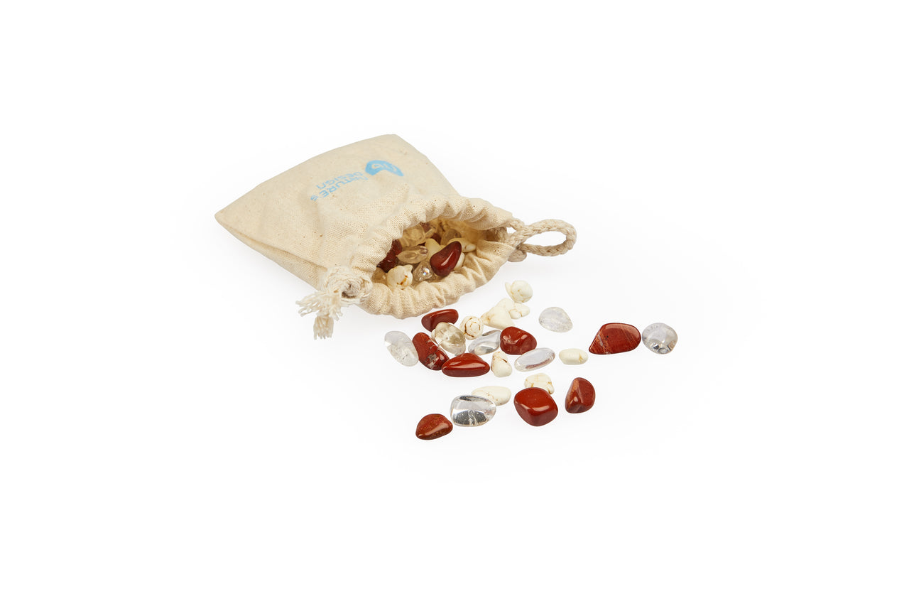 Ein cremefarbener Beutel mit Kordelzug, aus dem verschiedene polierte Edelsteine in Rot, Klar und Cremeweiß herausfallen.