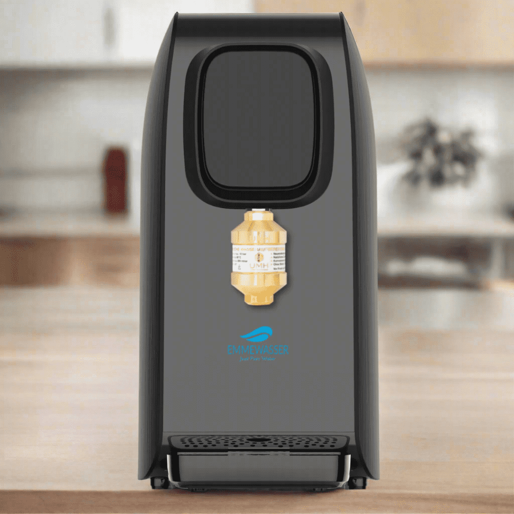 Ein schwarzer PureBliss + UMH Wasserenergetisierer mit goldenem Filteraufsatz, EmmeWasser-Logo, auf Holztisch in Küche.
