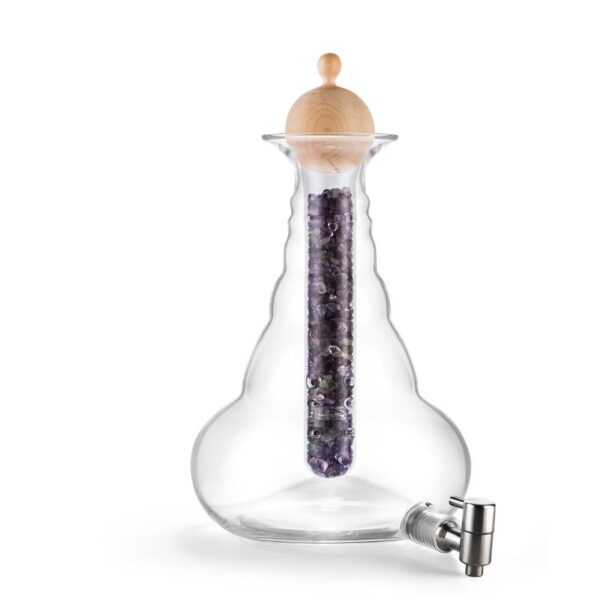 Eine große, bauchige Glas-Karaffe mit Holzdeckel und Ausgießer; innen ein Glasröhrchen mit violetten Steinen gefüllt.