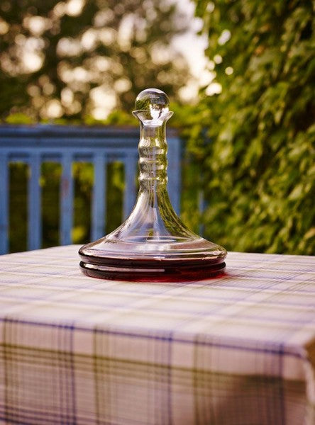 Auf einem karierten Tisch steht eine elegante, bauchige Rubellum Weinkaraffe aus Glas, teils mit Rotwein gefüllt.