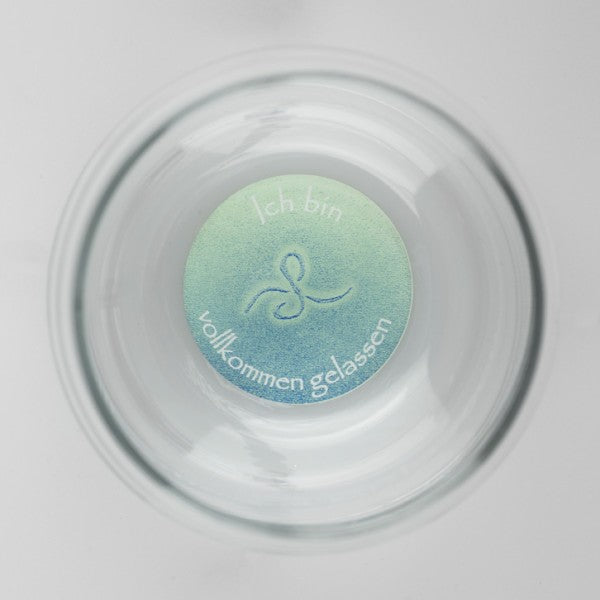 Ein transparenter Mythos Becher mit rundem Bodendesign, zartes Grün-Blau, Gravur „Ich bin vollkommen gelassen“ in Deutsch.