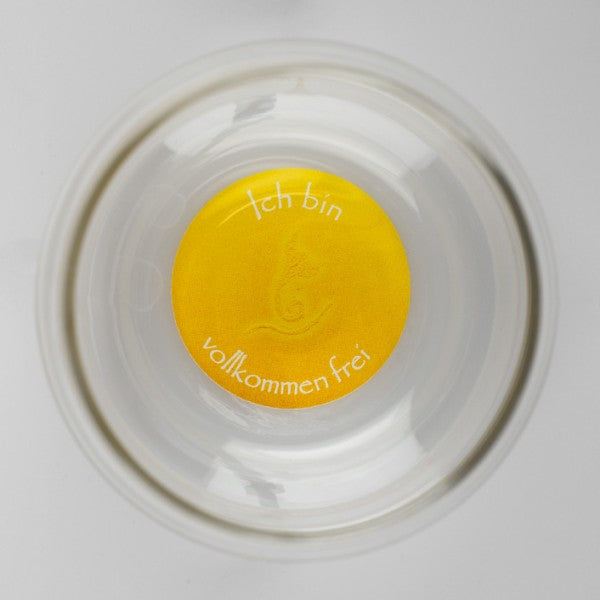 Ein transparenter Mythos Becher mit gelbem Boden, auf dem „Ich bin vollkommen frei“ in weißer Schrift auf Deutsch steht.