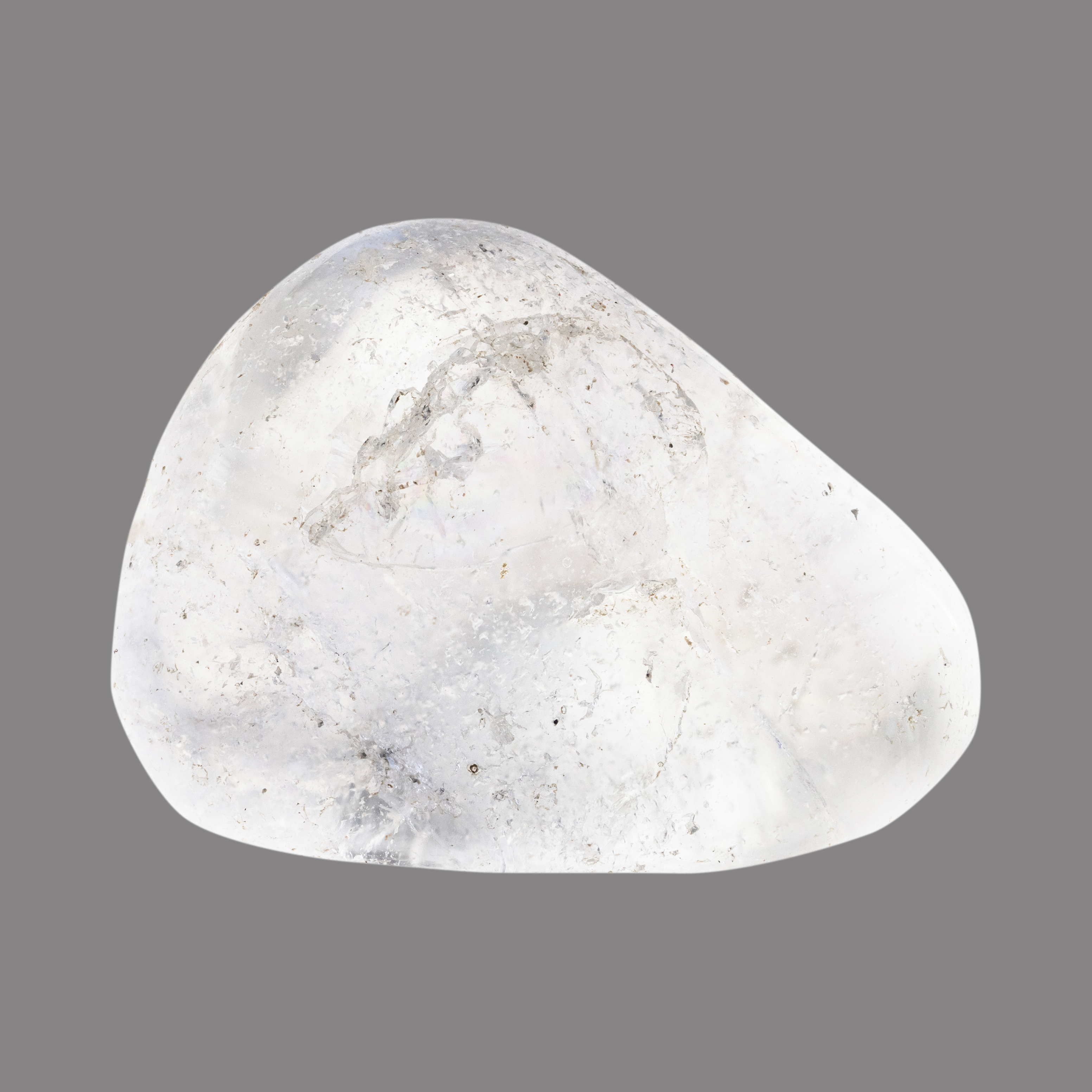 Ein transparenter, glatter, polierter Stein mit leicht unregelmäßiger Form und inneren Einschlüssen liegt vor grauem Hintergrund.