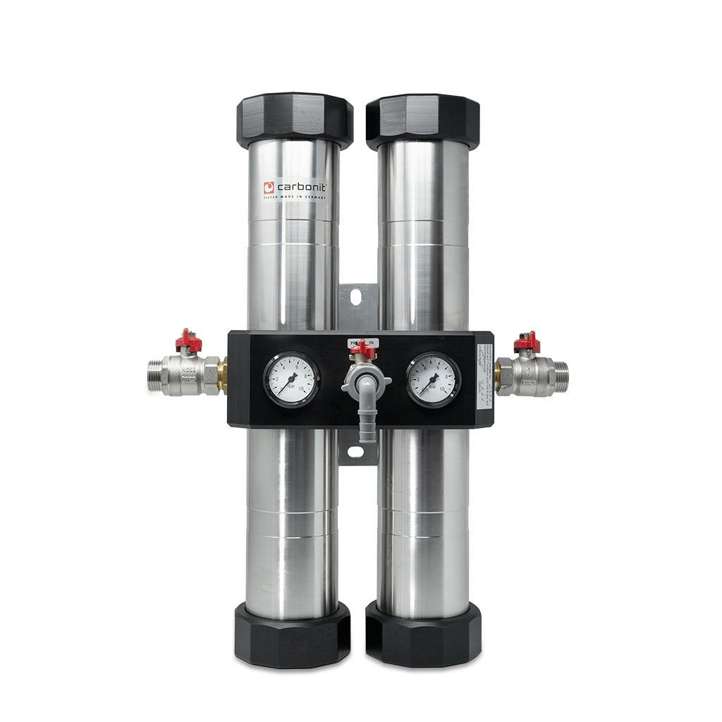 Das Bild zeigt eine Carbonit QUADRO Hausfilter-Anlage mit zwei Edelstahlzylindern, Manometern, Ventilen und Anschlüssen.