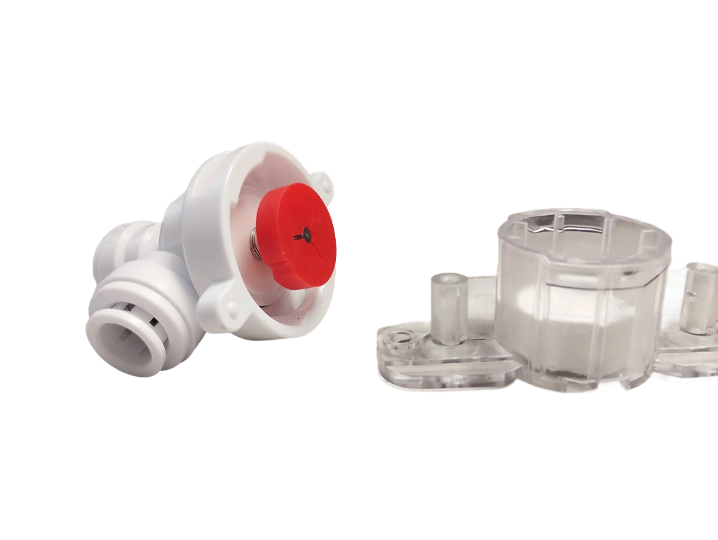 Links auf dem Bild befindet sich ein weißes Kunststoffbauteil mit rotem runden Mittelteil und sichtbarer Feder. Rechts daneben liegt ein durchsichtiges Kunststoffgehäuse mit zylindrischem Aufbau, in dem ein weißes, rundes Filter- oder Schwammelement zu sehen ist. Beide Bauteile scheinen Teil eines technischen oder sanitärtechnischen Geräts zu sein.