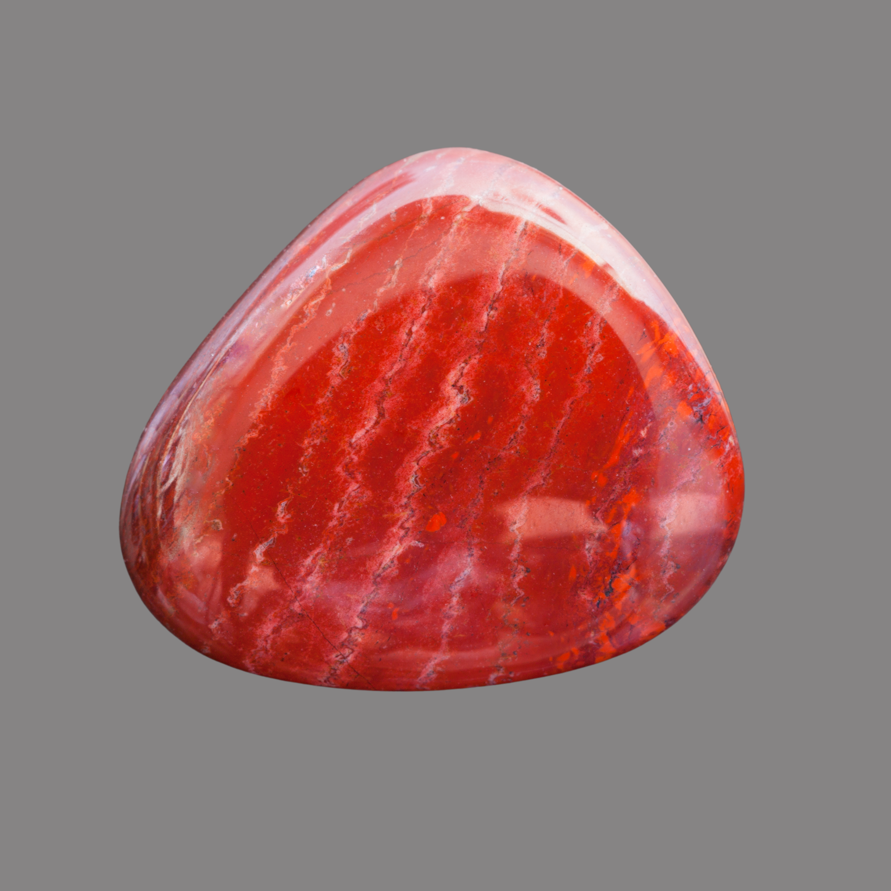 Im Bild ist ein glänzender, rot gemusterter Stein mit abgerundeter, polierter Oberfläche vor grauem Hintergrund zu sehen.