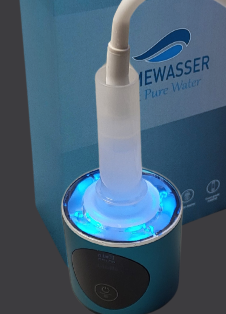 Das Bild zeigt ein blaues, zylindrisches Gerät mit einem beleuchteten, transparenten Bereich und einem angeschlossenen Schlauch. Am unteren Teil befindet sich ein Bedienfeld mit einem Ein-/Ausschalter. Im Hintergrund ist eine Verpackung in Blautönen zu sehen, auf der der Schriftzug „MEWASSER Pure Water“ und ein Logo mit einer stilisierten Wasserwelle abgebildet sind. Auf der Verpackung sind zudem mehrere kleine Symbole sichtbar, die vermutlich Produktmerkmale darstellen.
