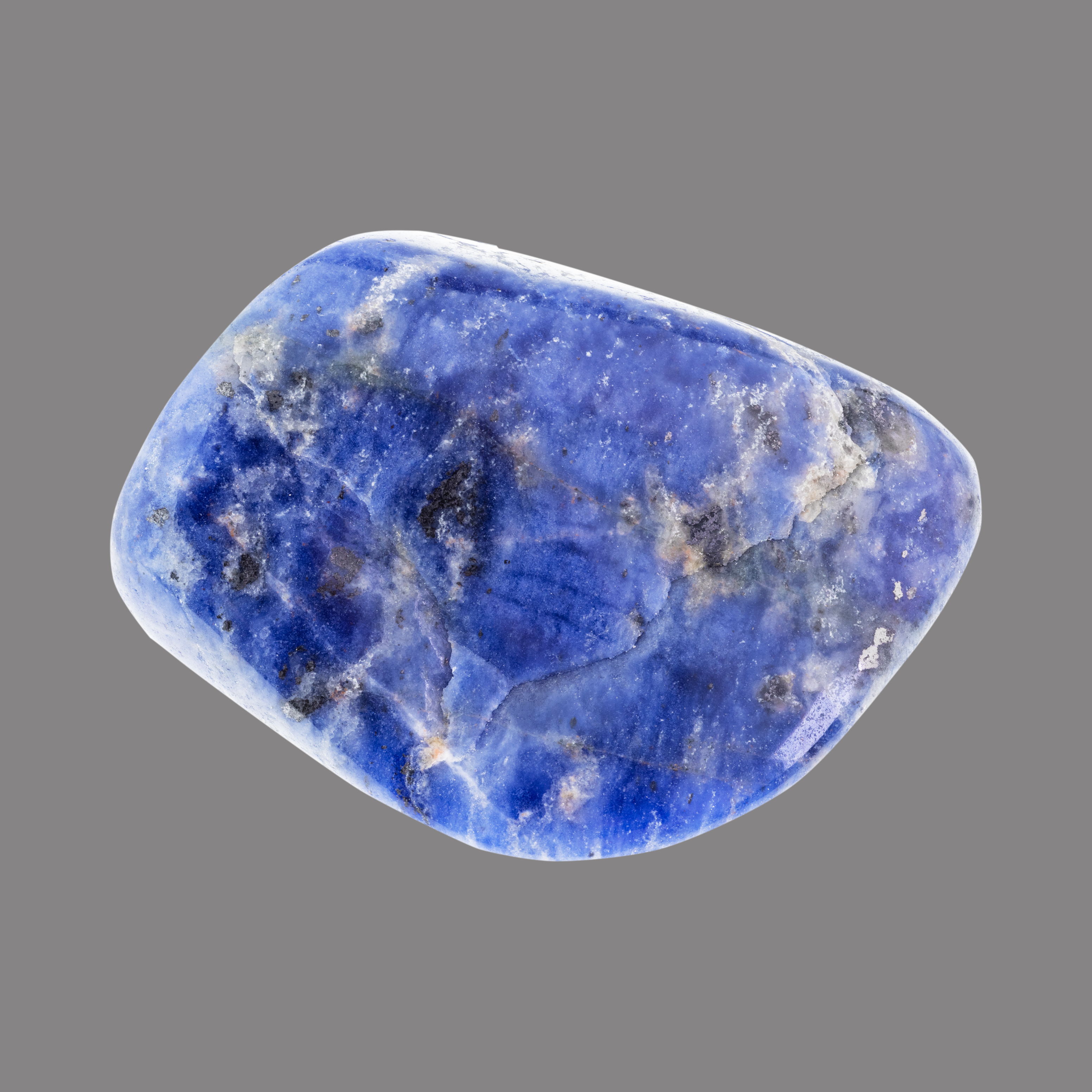 Ein glatt polierter, unregelmäßig geformter blauer Edelstein mit weißen und schwarzen Maserungen, vor grauem Hintergrund.
