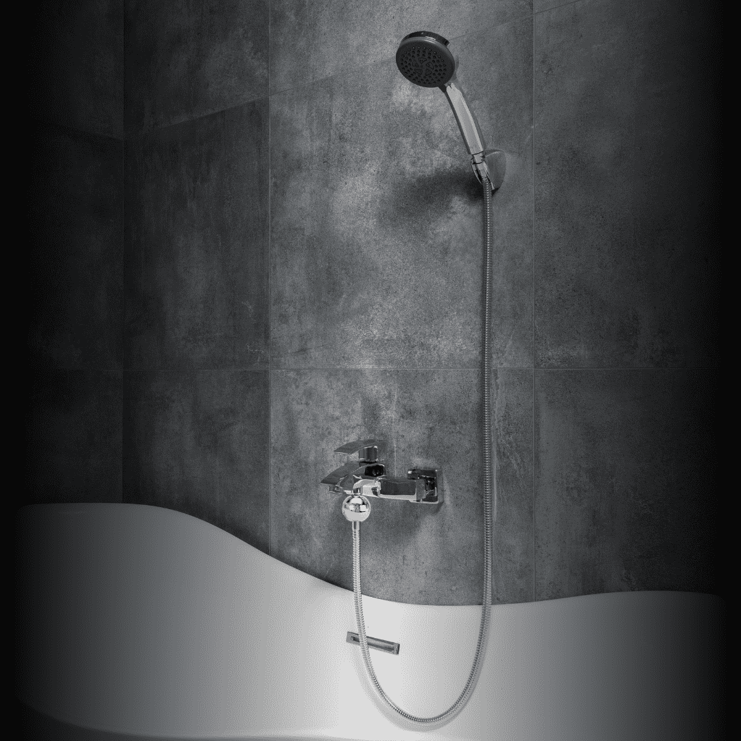 Eine moderne Badewanne mit geschwungenem Rand, Wandarmatur und einer silbernen Handbrause vor dunkelgrauen Fliesen.