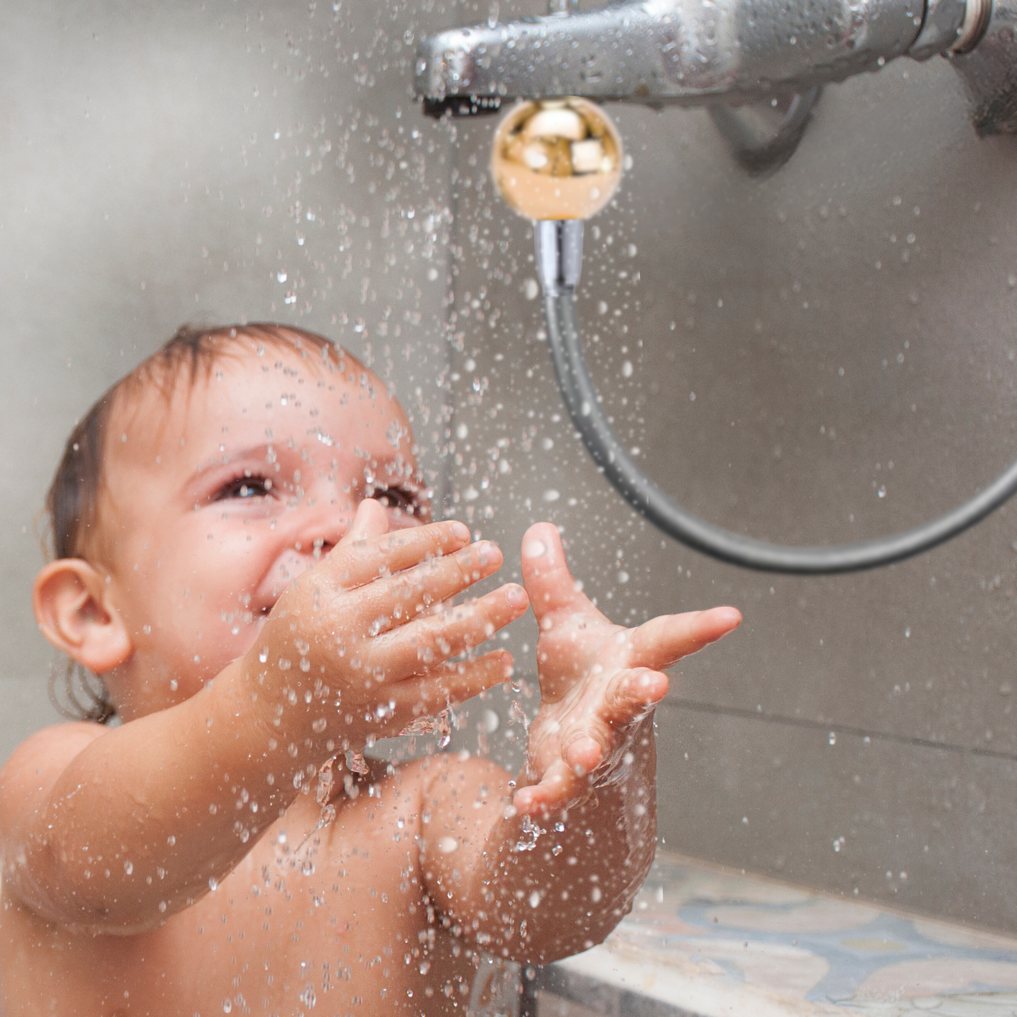 Ein lachendes Kleinkind spielt fröhlich mit spritzendem Wasser unter einem Wasserhahn mit flexiblem Verlängerungsschlauch.