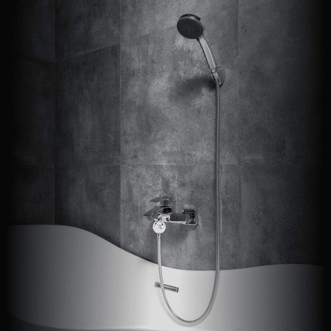 An einer Wand mit dunklen, grauen Fliesen ist eine moderne Handbrause mit flexiblem Metallschlauch angebracht. Darunter befindet sich eine glänzende Chrom-Armatur mit Mischbatterie, die auf einem weißen, geschwungenen Badewannenrand installiert ist. Die Szenerie wirkt schlicht und elegant, mit Fokus auf den Kontrast zwischen der weißen Badewanne und den dunklen Wandfliesen. Es sind keine weiteren sichtbaren Gegenstände, Dekorationen oder Pflegeprodukte im Bild, alles wirkt sauber und minimalistisch.