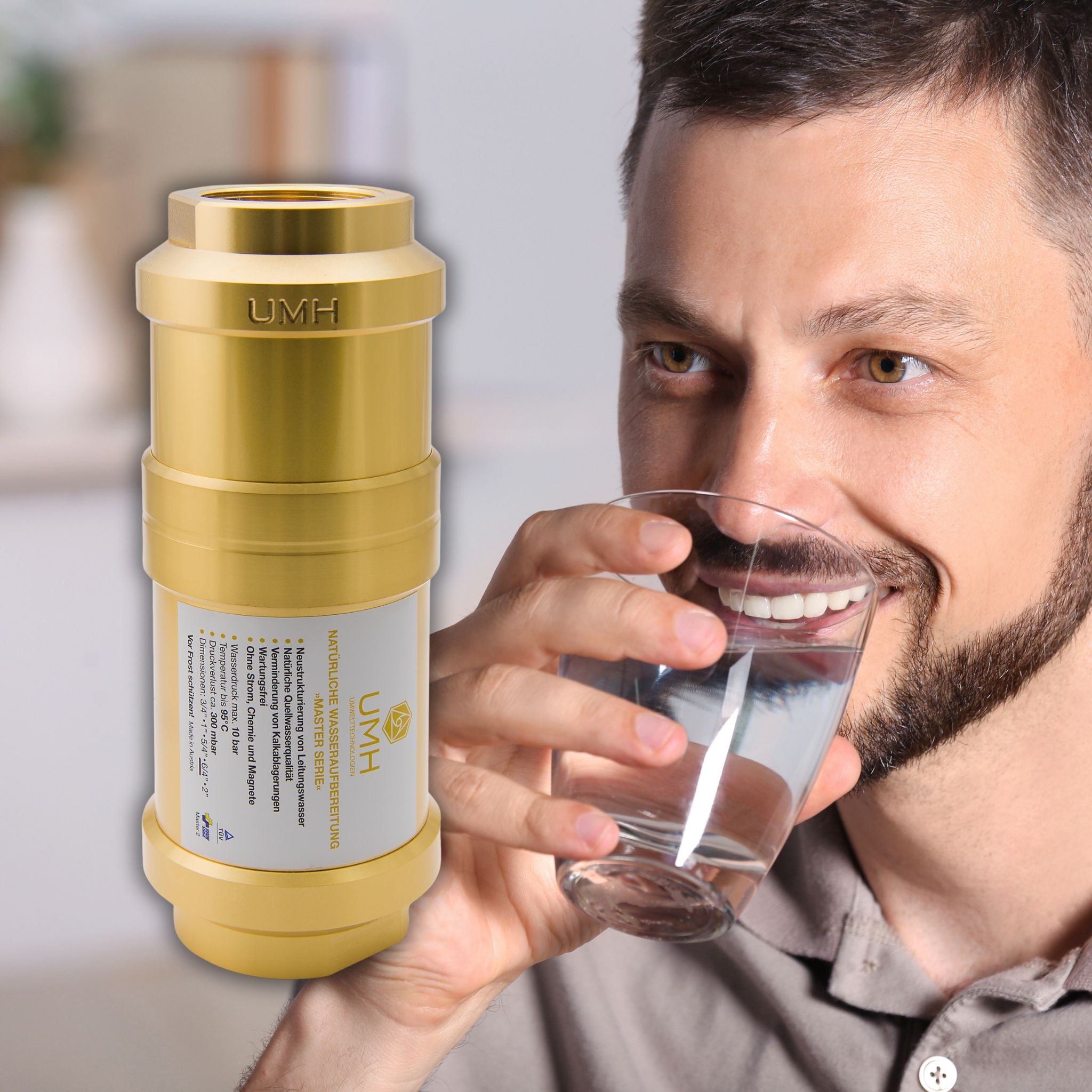 Ein Mann mit braunem Haar und Bart trinkt aus einem klaren Glas Wasser, daneben ein goldener UMH Wasserfiltergerät.