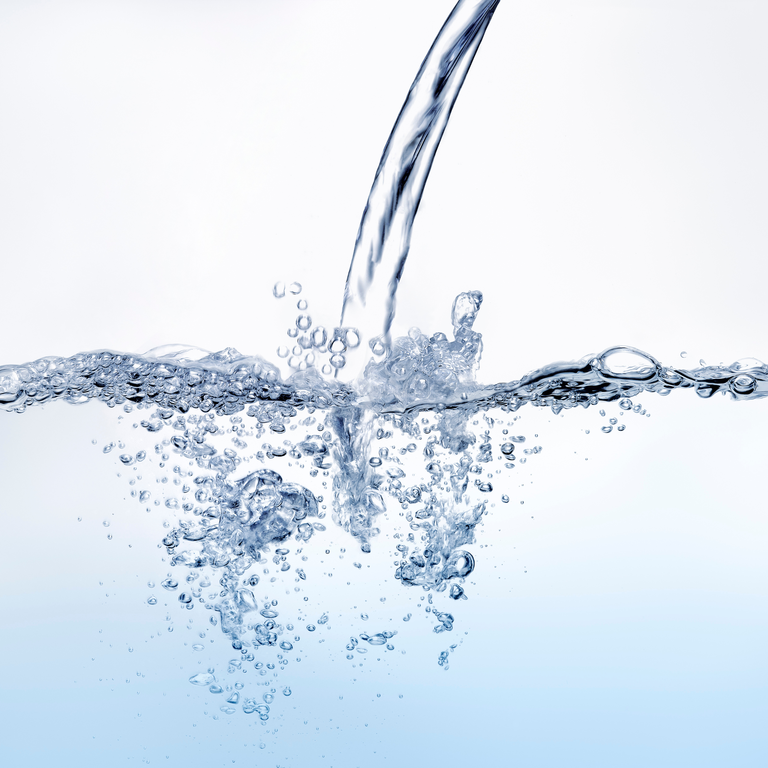 Ein klarer Wasserstrahl fließt von oben in transparentes Wasser, zahlreiche Luftblasen steigen auf, helle Hintergrundfarbe.