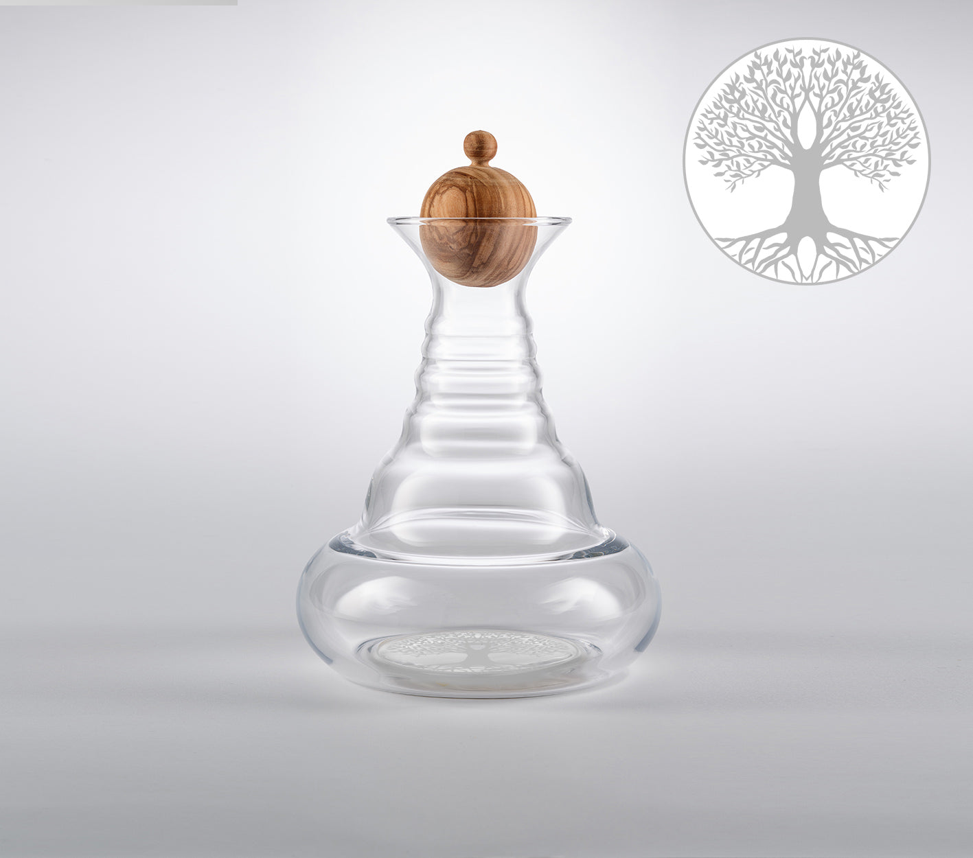 Eine klare, bauchige Alladin Karaffe aus Glas mit einem runden Holzverschluss, auf weißem Hintergrund, Baum Motiv im Hintergrund.