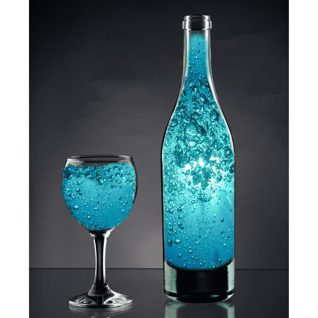 Eine klare Glasflasche und ein Weinglas, beide mit sprudelndem, leuchtend blauem Getränk und aufsteigenden Blasen gefüllt.