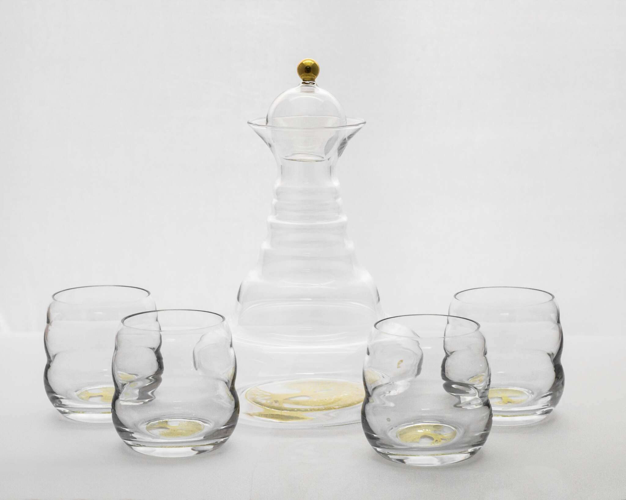 Eine elegante Glaskaraffe mit goldenem Deckel und goldfarbenem Lebensbaum-Motiv, umgeben von vier passenden Trinkgläsern.