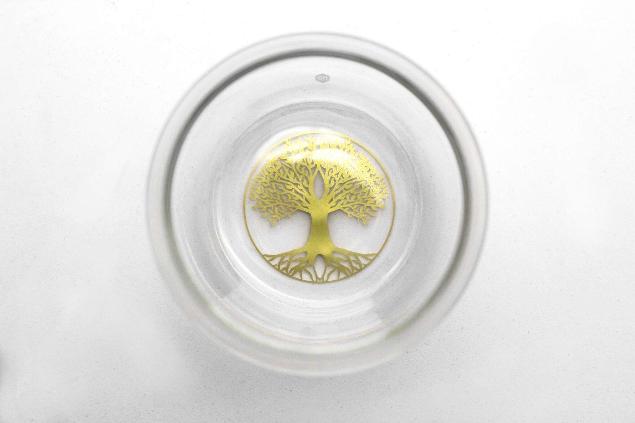 In der Mitte eines transparenten Glases ist ein goldfarbener Lebensbaum mit verzweigten Ästen und Wurzeln zu sehen.
